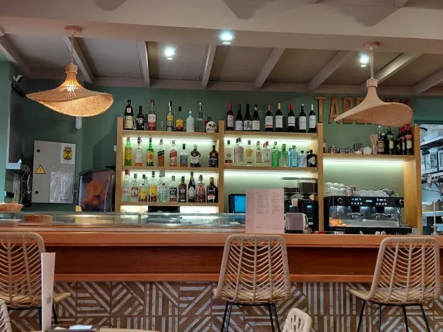 A bar counter with lit bottle shelves, wicker lamps and high stools