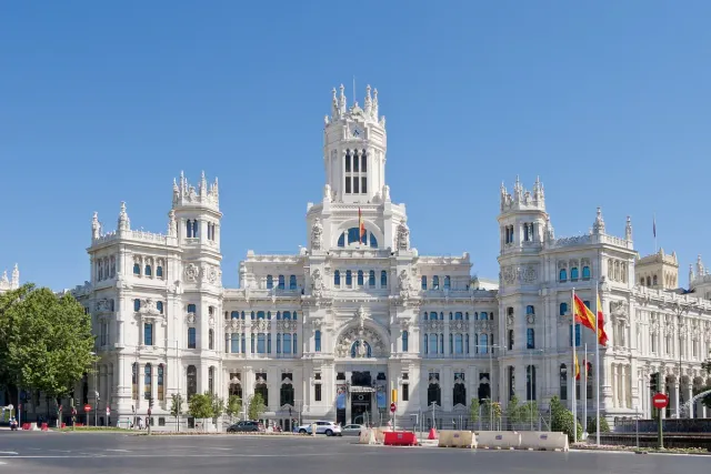 A monumental white palace with towers and pointed spires facing a busy square