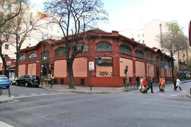 A red brick covered market building with arched windows on a street corner