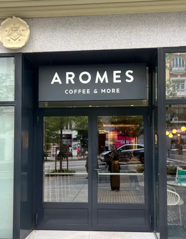 An entrance with glass doors and a dark sign, the street reflected in the windows