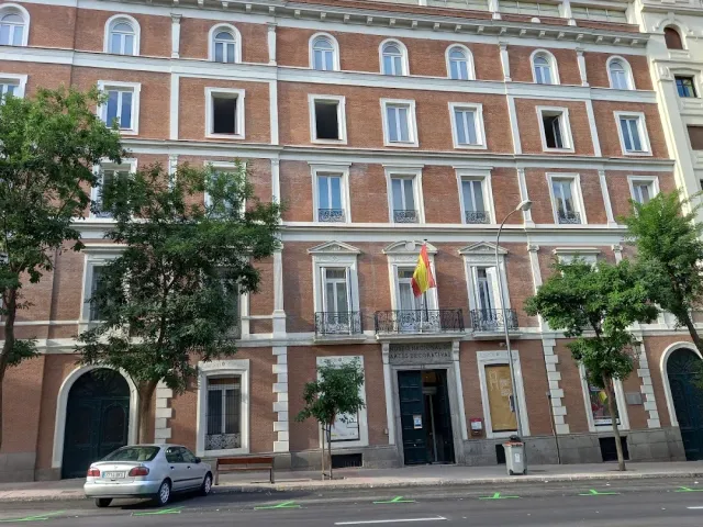 A multi storey red brick facade with iron balconies and a flag above the entrance