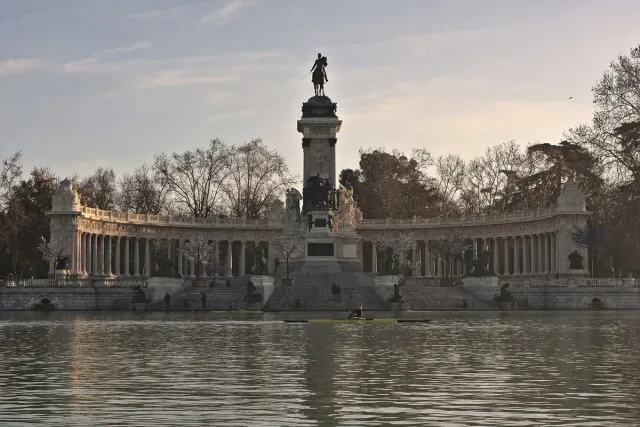 A monument with a semicircular colonnade and an equestrian statue at its centre on a park lake shore