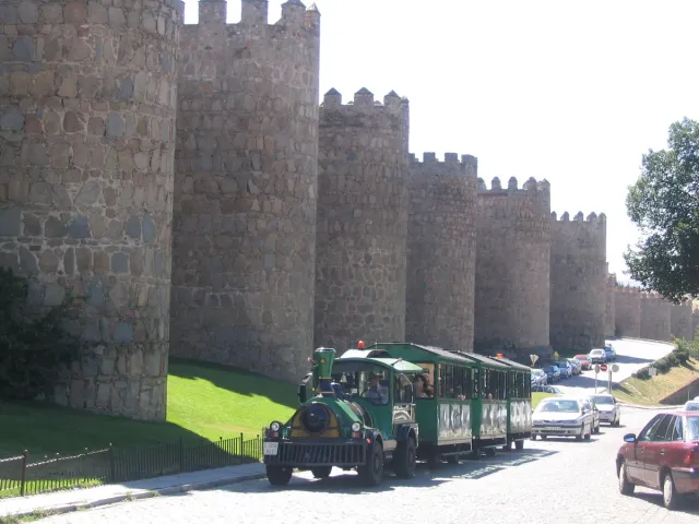 A long fortified wall with round towers and crenellations, with a road and a tourist train at its foot