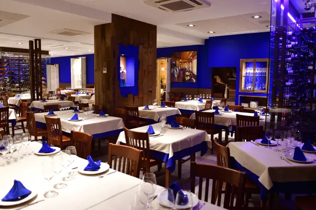 A dining room with blue walls, white cloths with blue napkins and wine racks