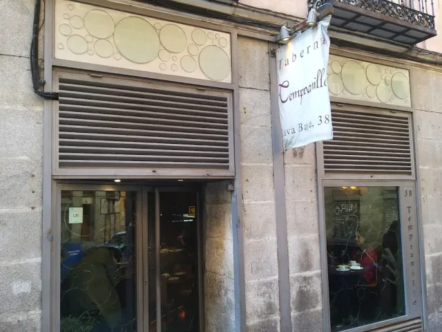 A stone facade with a hanging sign, half lowered shutters and windows with decorated glass