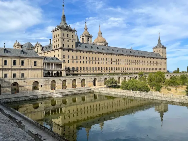 A long stone building with spires and domes, reflected in a rectangular pond