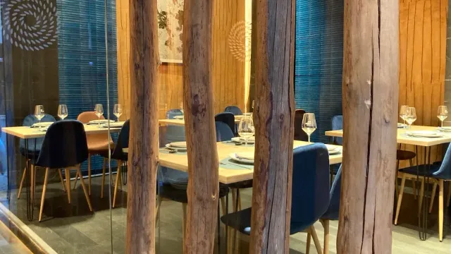 A restaurant interior seen through glass with rough wooden posts, laid tables and blue chairs