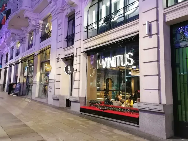 A lit facade at night with large glass windows and diners inside, on a paved street