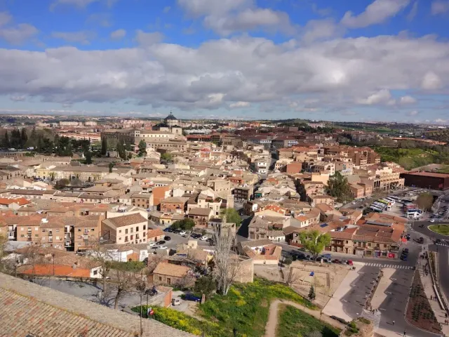A view from above over the tiled rooftops of a town, with hills and a cloudy sky on the horizon