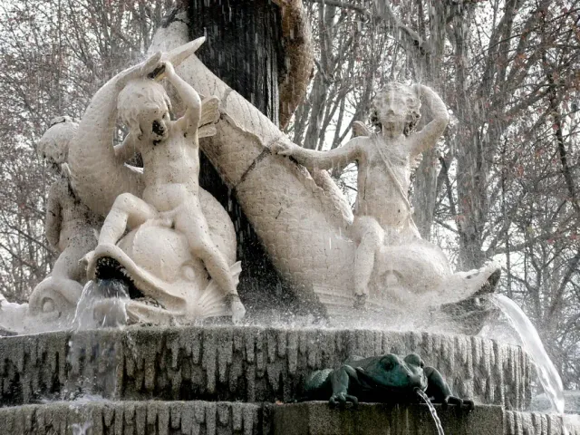 Stone sculptures of children and turtles on a fountain, covered in icicles