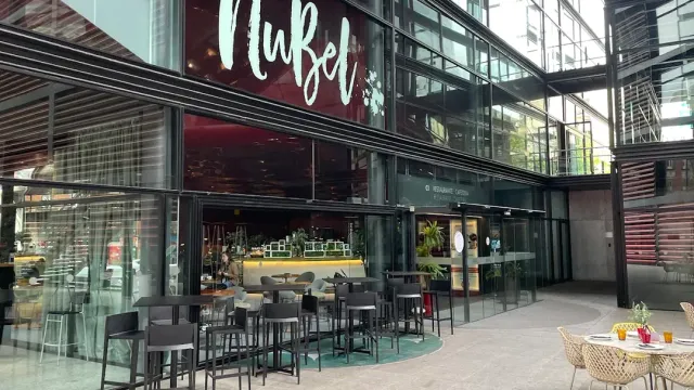 A tall glass facade with sign lettering, and high tables and bar stools outside