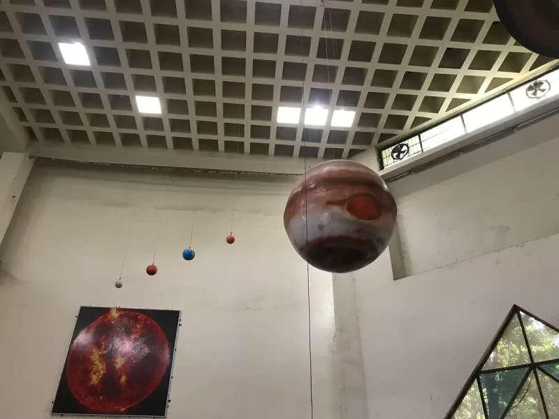 Model planets hanging on wires from the ceiling of a museum hall, with a photograph of the sun on the wall