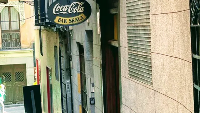 A narrow paved alley with a round bar sign hanging above old facades