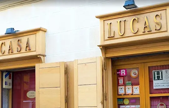 A wooden shop front with gilded letters on the sign, and closed wooden shutters at the entrance