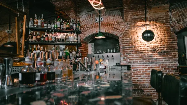 A bar with a brick arch, bottle shelves and a shiny marble counter in dim light