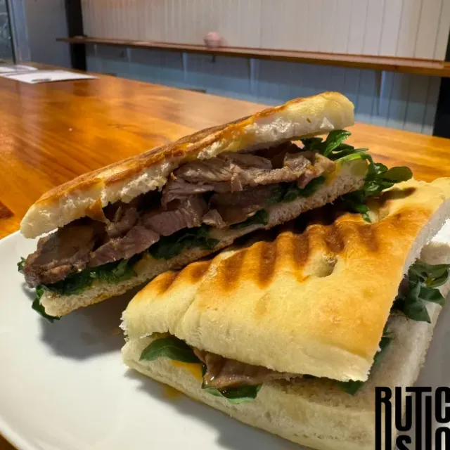 Two halves of a grilled flatbread sandwich with sliced meat and green leaves on a plate