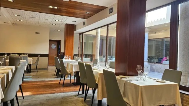 A dining room with cream coloured cloths, olive chairs and dark wooden columns by the windows