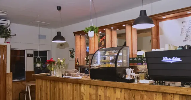A long wooden counter with a dessert case, an espresso machine and hanging black lamps