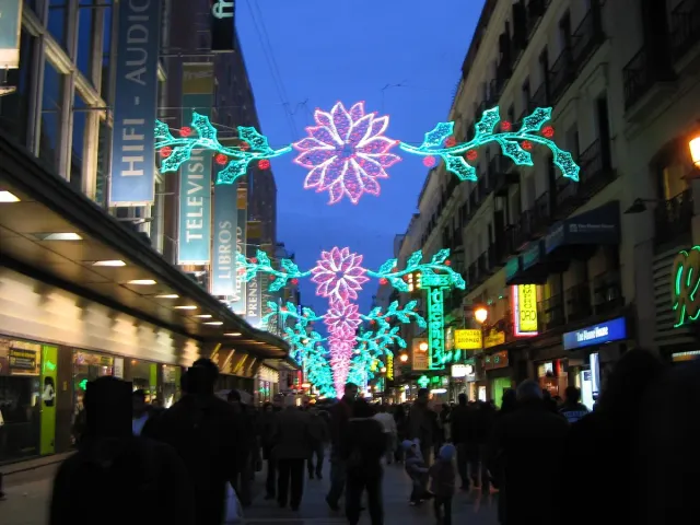 A busy shopping street at night with flower shaped light decorations hanging above the crowd