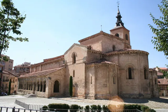 A pale stone Romanesque church with an arcaded porch along its side and a bell tower
