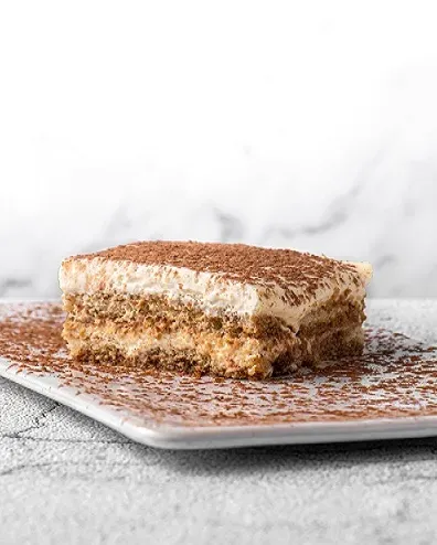 A slice of layered dessert with white cream and cocoa powder on a square plate