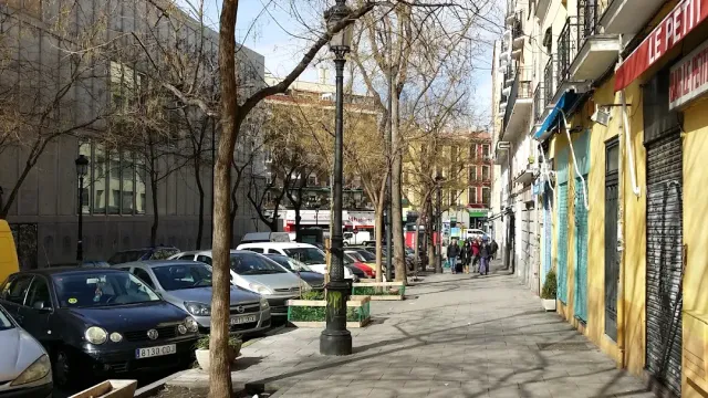 A neighbourhood street with parked cars, bare trees and an iron lamp on a wide pavement