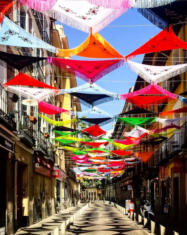 A narrow street shaded by a canopy of colourful parasols strung between the buildings