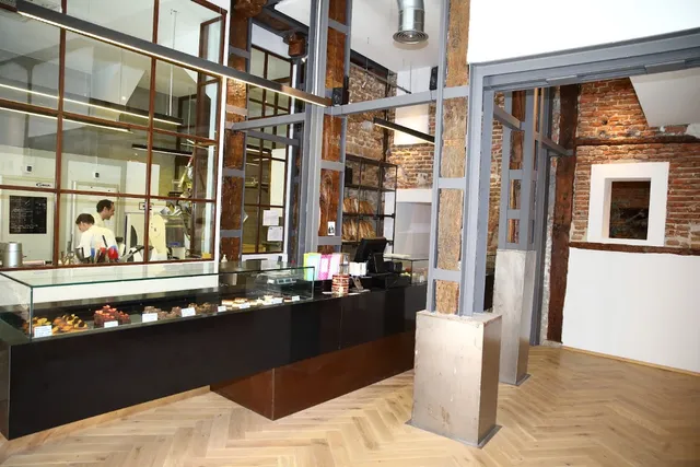 A long cake display case between steel beams and exposed brick walls