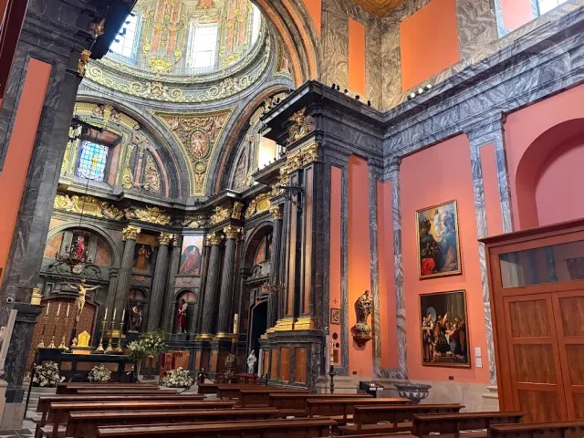A church interior with orange walls, dark marble columns, a painted dome and wooden pews