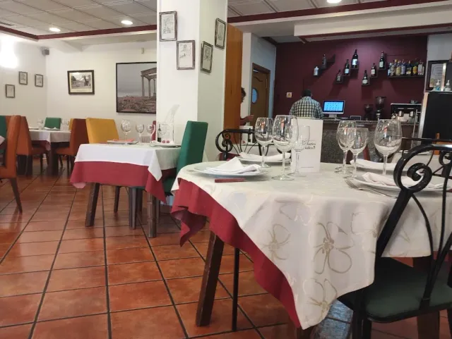 A dining room with a reddish tiled floor, white and red tablecloths and colourful chairs