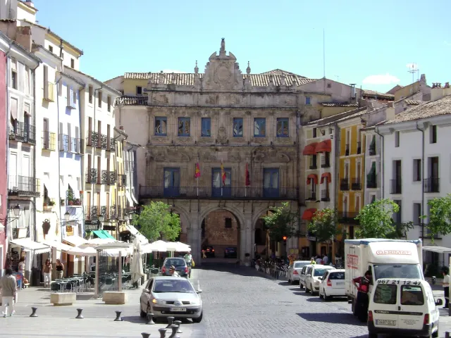 A narrow square ringed by colourful balconied houses, terrace parasols and an arcaded building at one end