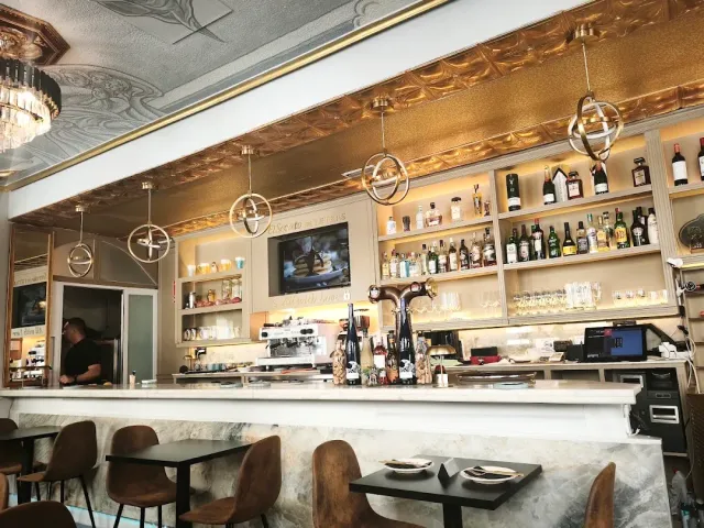 A long marble counter with hanging lamps, shelves of bottles and a coffee machine behind it