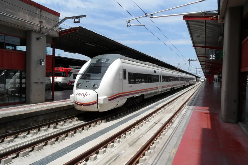 A white Renfe passenger train standing at a covered railway station platform beside a platform 16 sign