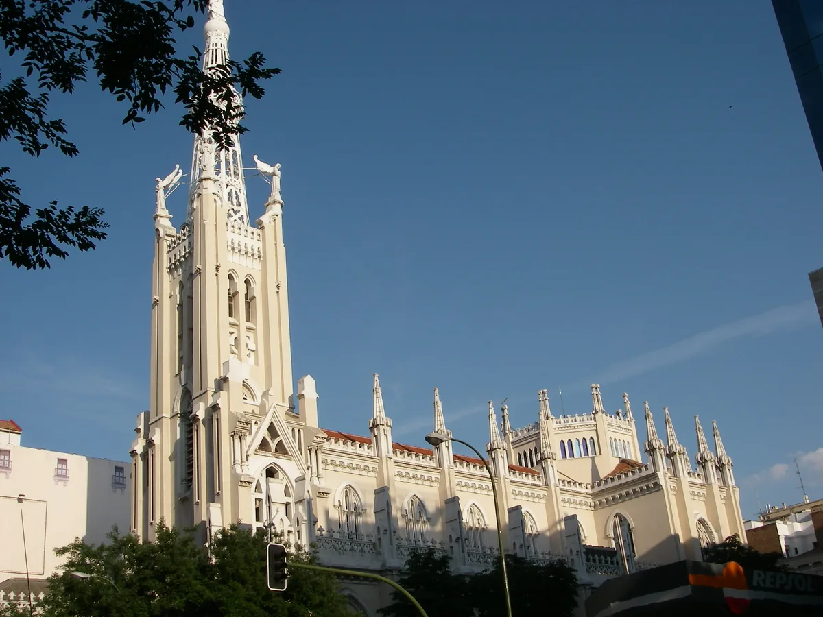 A white neo gothic church with a tall spire and pinnacles along the roof against a clear blue sky