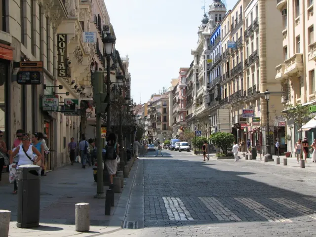 A sloping street lined with stone buildings, pedestrians and a row of street lamps