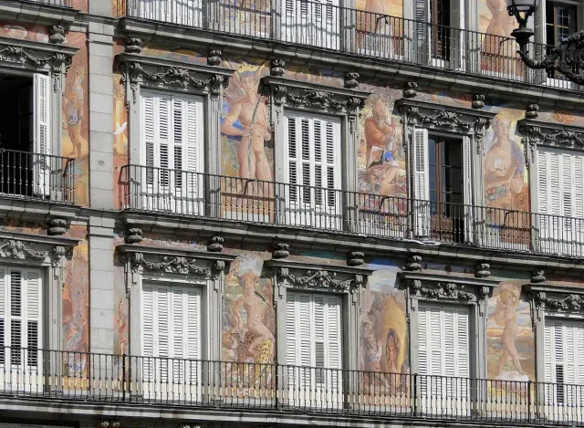 A facade painted with frescoes of figures and patterns, with a row of iron balconies