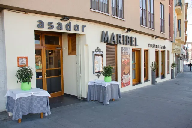 A pale restaurant facade with wooden doors and small tables with potted plants on the sidewalk