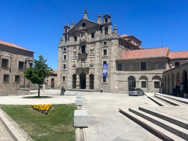 A grey stone church facade with a sculpted portal, facing an empty square and a flower bed