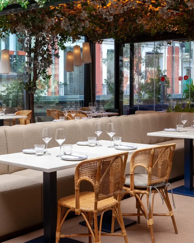 Set marble tables with wicker chairs, an upholstered bench and greenery hanging from the ceiling