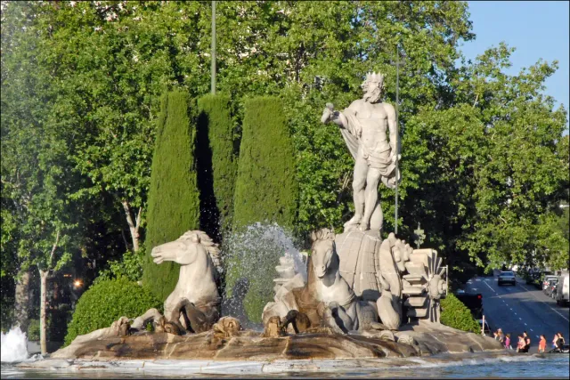 A fountain with a marble statue of a sea god on a chariot drawn by sea horses, ringed by clipped hedges