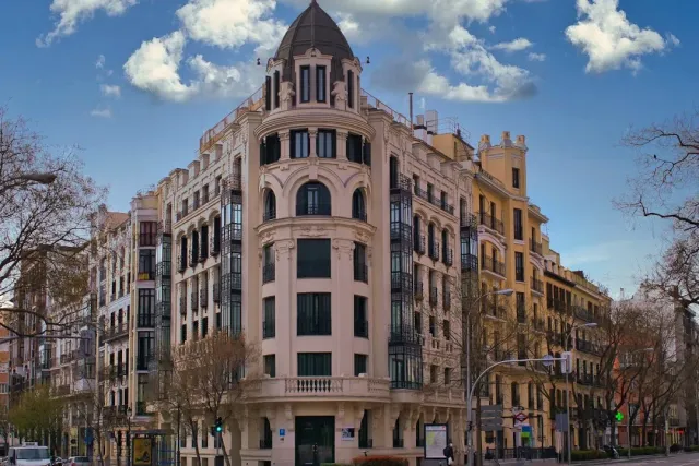 A corner building with a small dome on top and iron balconies, under a sky with clouds