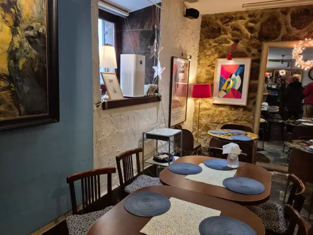 A dining room with a stone wall, framed pictures and wooden tables with blue placemats