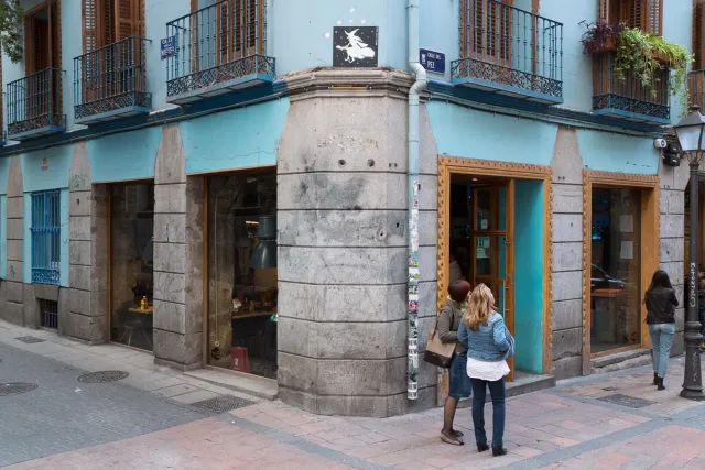 A street corner with a turquoise painted bar front, shop windows and an enamel street sign