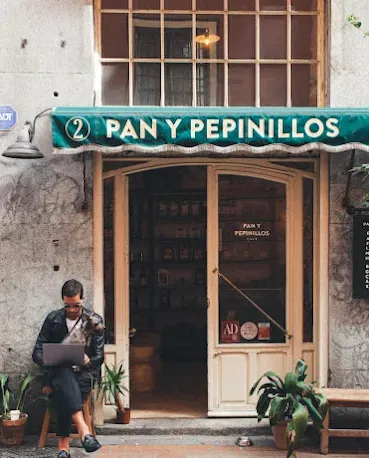 A shopfront with a green awning and a woman sitting outside with a laptop