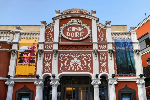 An ornate cinema facade in pale plaster and red paint, with a rounded lettered sign above the entrance
