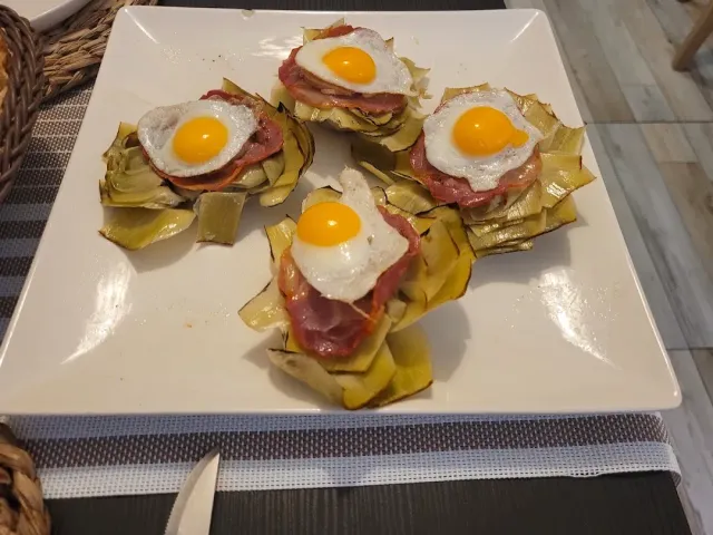 Four artichoke nests topped with a slice of meat and a fried egg on a square white plate