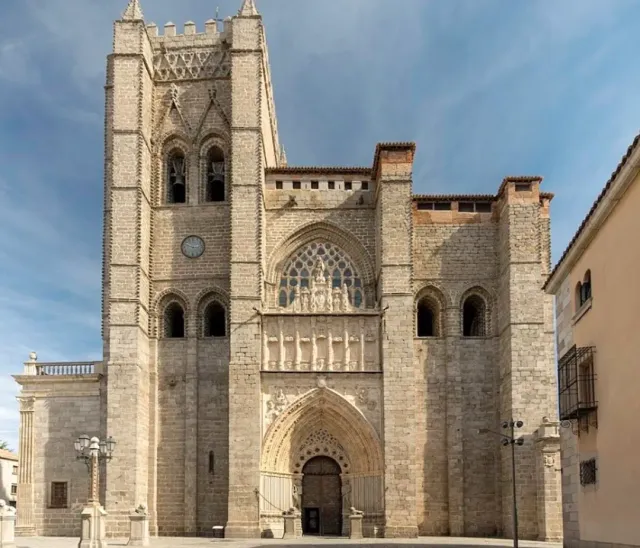 A Gothic stone facade with a fortified tower, a pointed portal and a round window above it