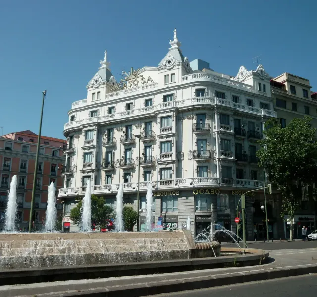 An ornate white corner building with a small dome facing a busy city junction