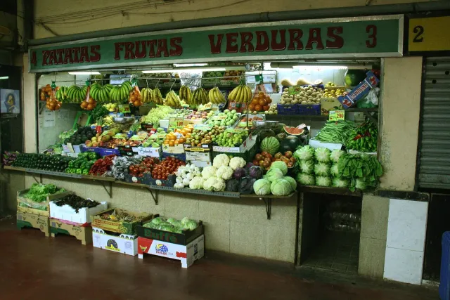 A fruit and vegetable stall in a covered market, with colourful crates and a sign above