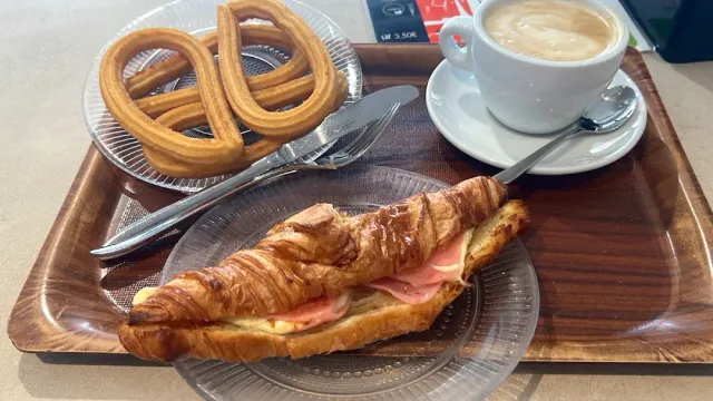 A tray with a loop of churro, a croissant filled with meat and cheese and a cup of coffee